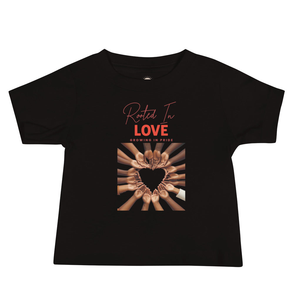 Black baby t-shirt with hands in varying shades forming a heart, captioned “Rooted in Love, Growing in Pride,” celebrating unity and pride.